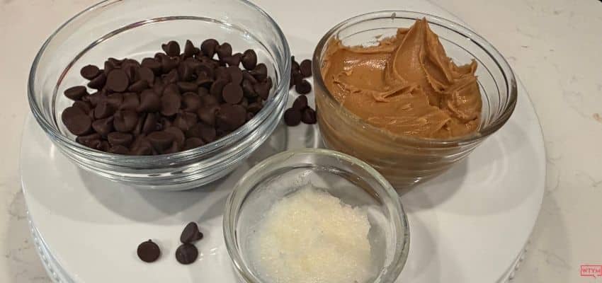 sugar free chocolate chips, natural peanut butter and coconut oil in glass bowls on a white cake stand