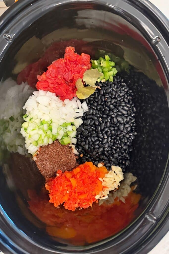 Dried black beans, diced peppers, onion, celery, garlic, diced tomatoes, spices and bay leaves in a crockpot for vegan black bean soup