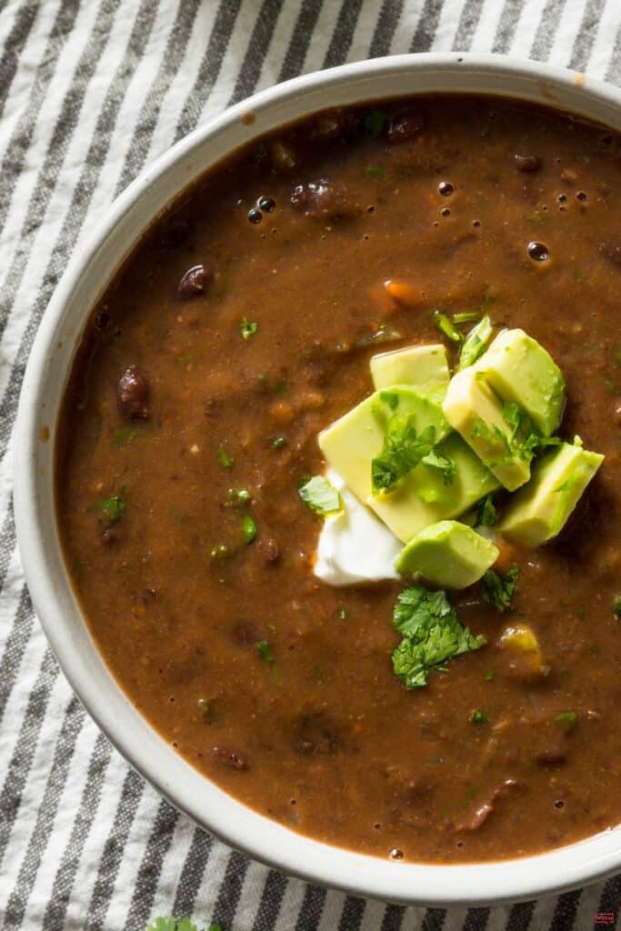 Bowl of vegan crockpot black bean soup topped with diced avocado, sour cream and fresh cilantro
