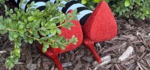 DIY witch legs with striped tights and red glitter ruby slippers lying in mulch against a brick house, like the Wizard of Oz witch under the house